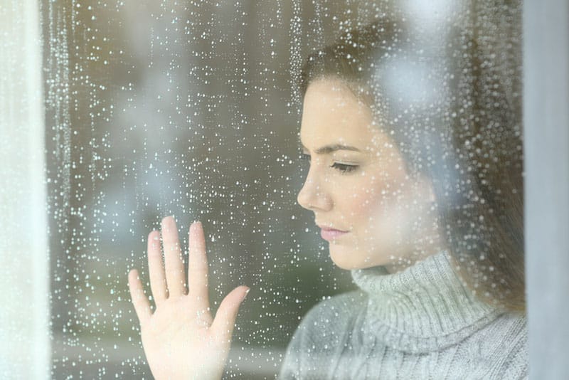 mulher triste a pôr a mão numa janela chuvosa