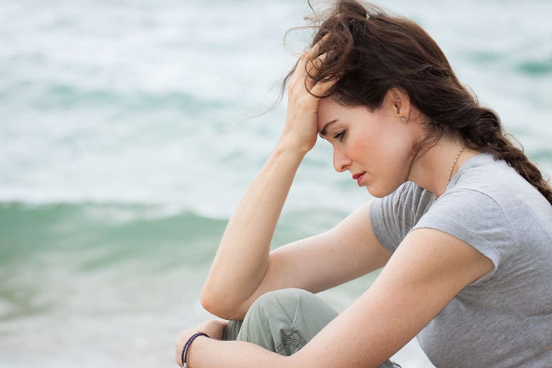 mujer triste sentada junto al mar