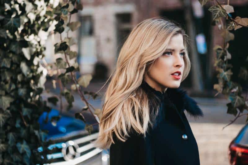 serious woman with black coat beside green vines