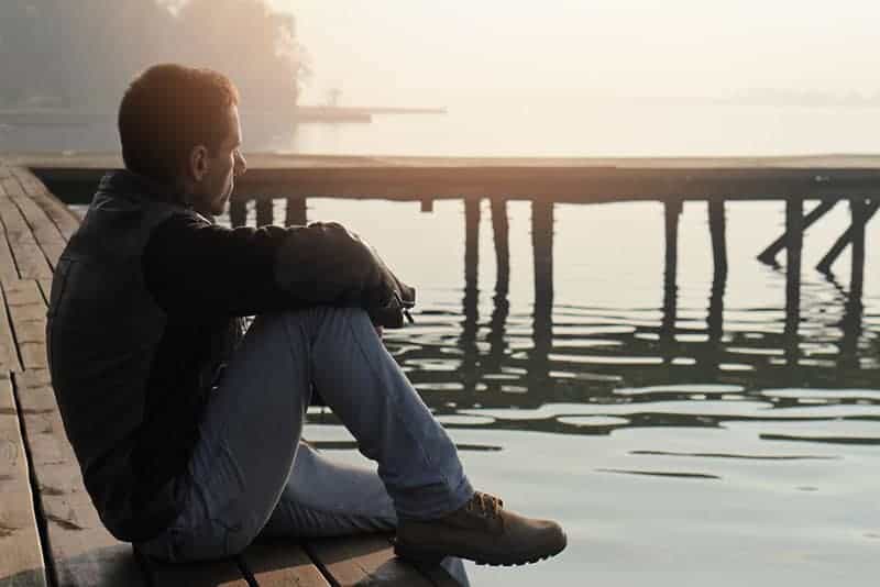 side view of man sitting on wooden dock beside water