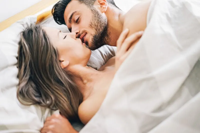 smiling man kissing with woman in bed