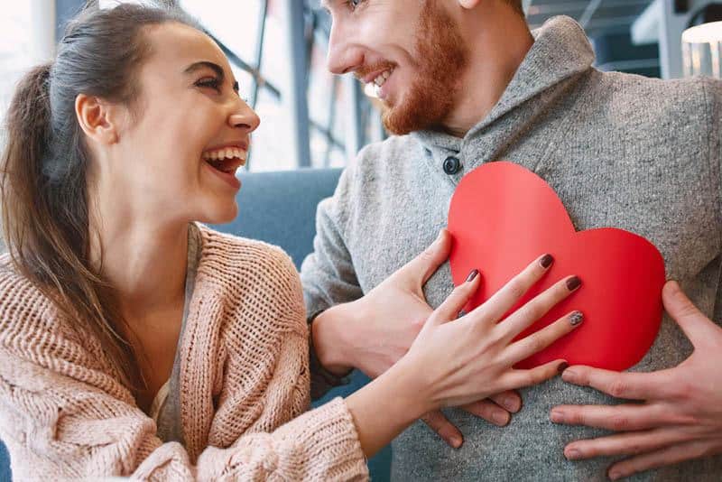 smiling woman giving her man a paper shape of heart