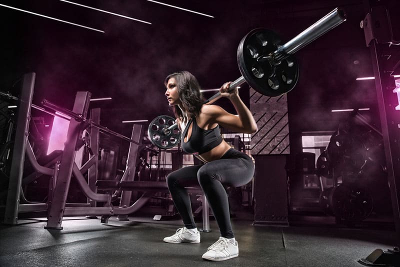 mujer haciendo sentadillas con barbel en el gimnasio