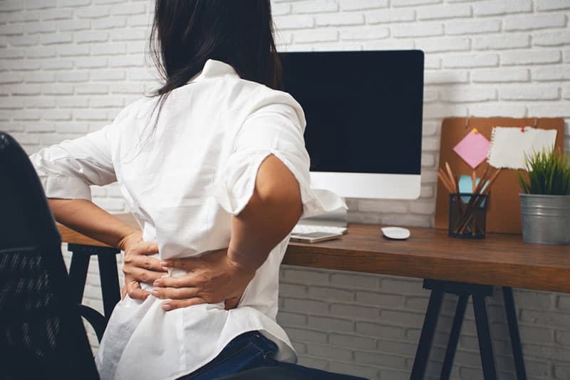 woman having back pain while sitting on chair