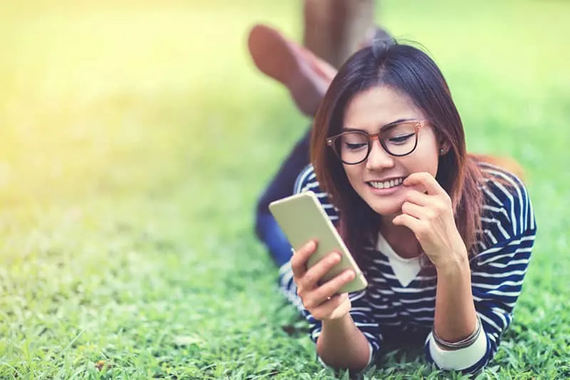 woman lying on grass and typing on phone
