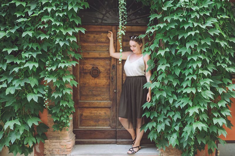 mujer de pie delante de puertas de madera junto a hojas