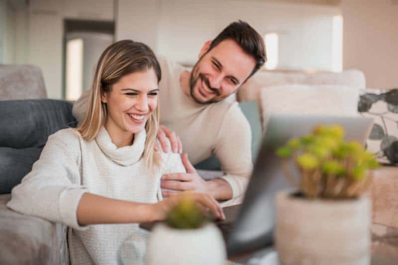 young happy couple sitting in living room and typing on laptop