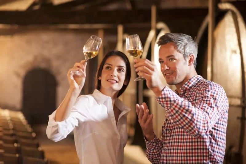 Couple enjoying a glass of white wine in a traditional cellar surrounded by wooden barrels.