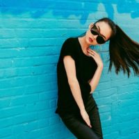 mujer con gafas de sol y posando apoyada en una pared azul