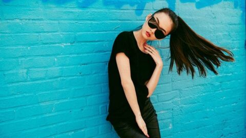 woman wearing sunglasses and posing while leaning on blue wall