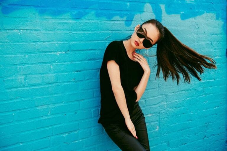 woman wearing sunglasses and posing while leaning on blue wall