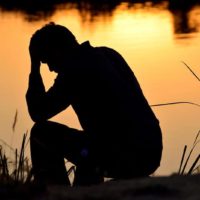 sad man sitting by the lake