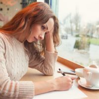 sad woman writing a letter in cafe