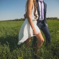 man holds woman waist while walking on grass field