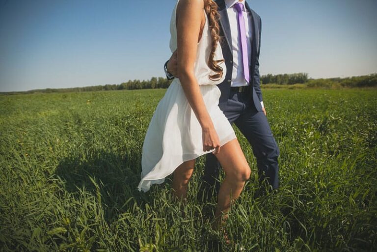 man holds woman waist while walking on grass field