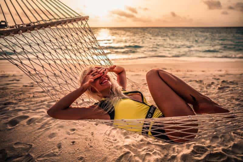 Woman in yellow bikini lying on hammock on the beach during the day