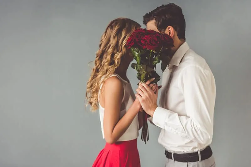 a man and a woman covered their faces with a bouquet of roses