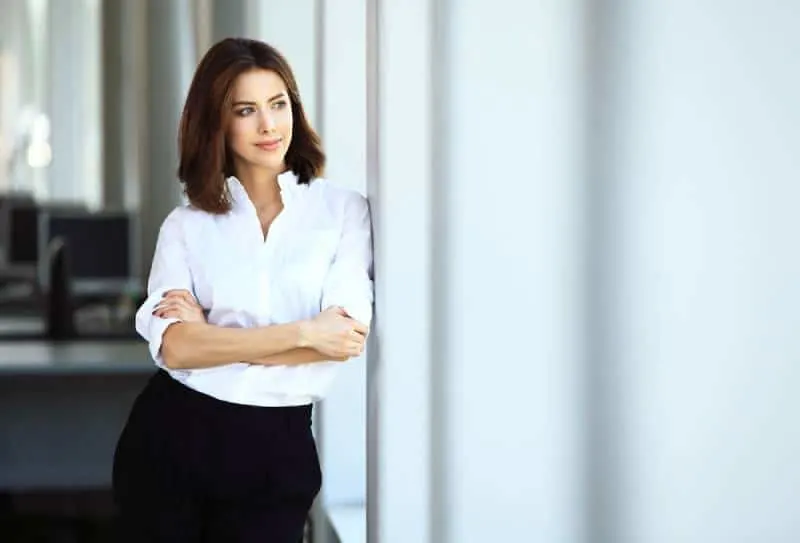 business woman in white shirt with crossed arms standing beside window