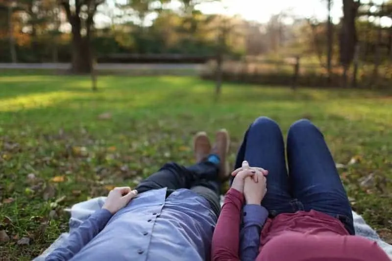 couple holding hands while lying on grass
