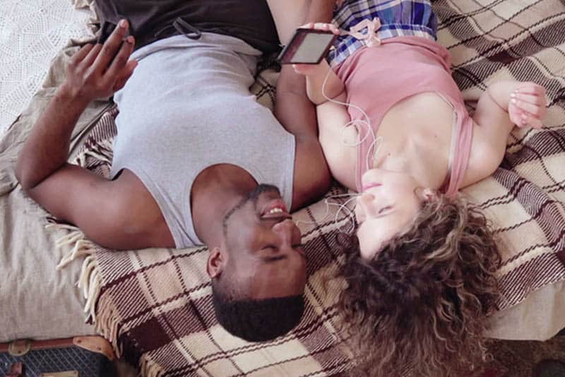 couple lying on bed while listening music