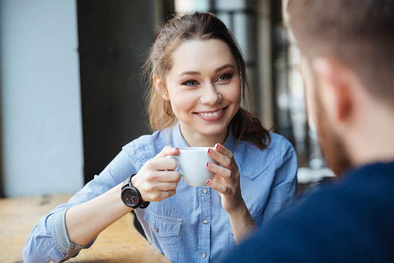 linda mujer sonriente sosteniendo una taza de café y mirando a un hombre