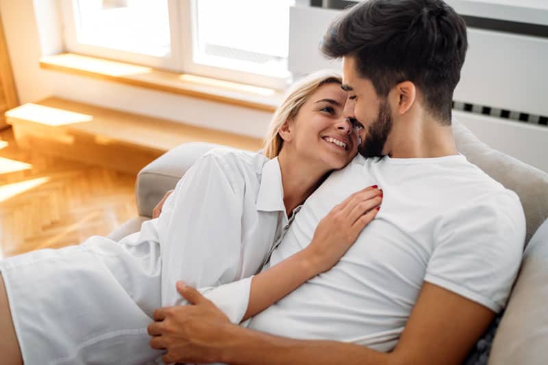 lovely couple lying on couch and looking each other at home