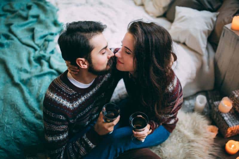 casal amoroso sentado na cama e a segurar um copo de vinho