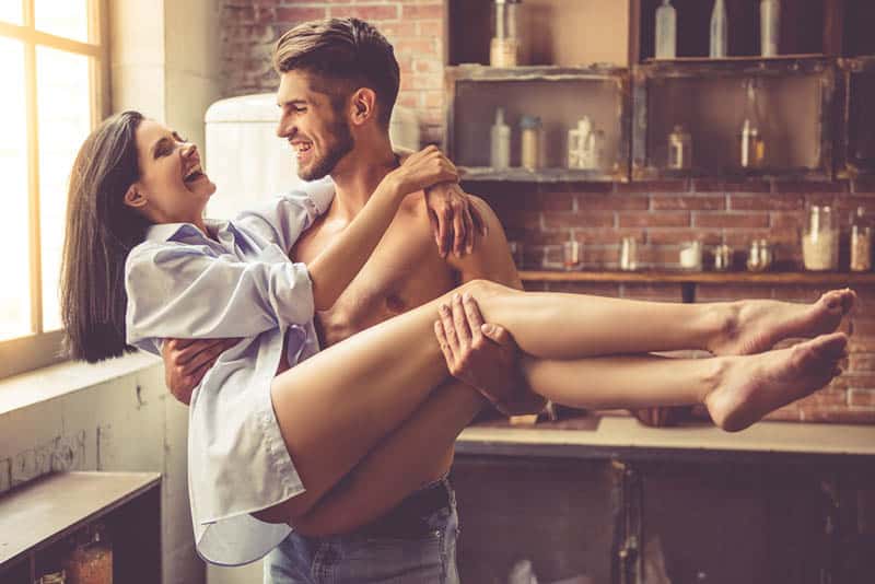 man holding smiling woman in arms at home