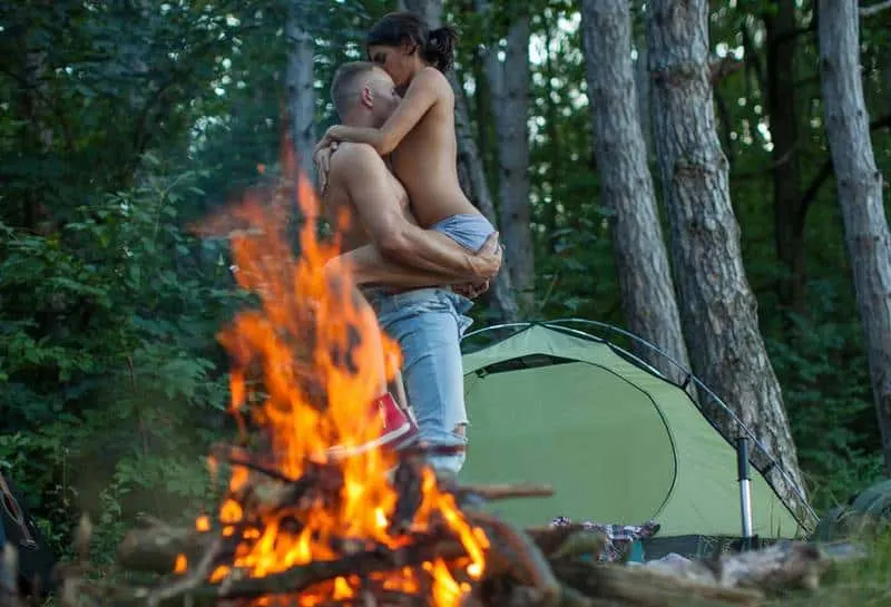 man holding topless woman in nature beside bonfire