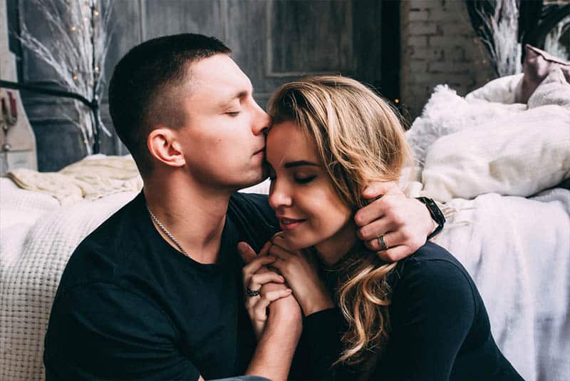 man kissing woman forehead in bedroom