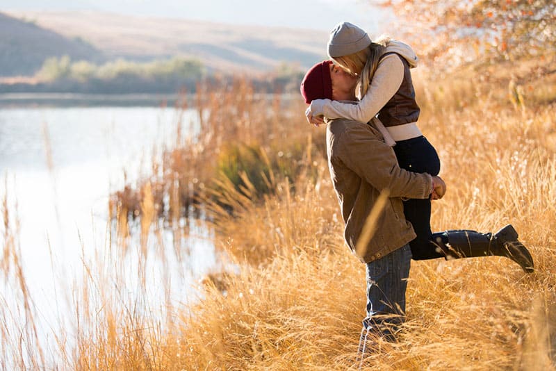 l'uomo prende in braccio la donna e la bacia in riva al lago