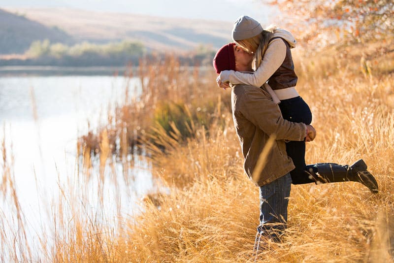 homem pega numa mulher e beija-a junto ao lago