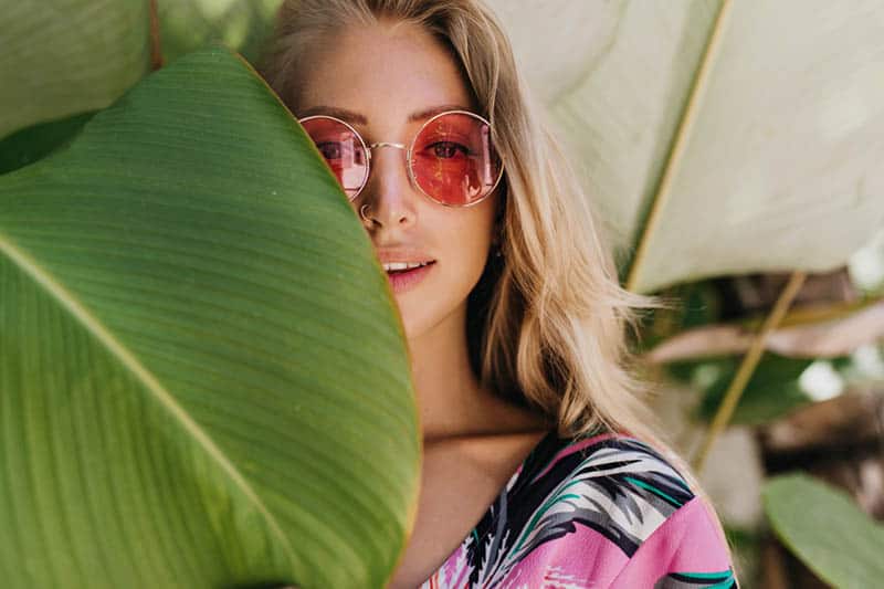 portrait of woman with red sunglasses standing beside leaf