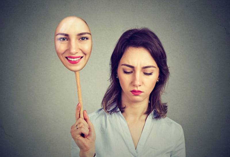 sad woman holding smiling mask