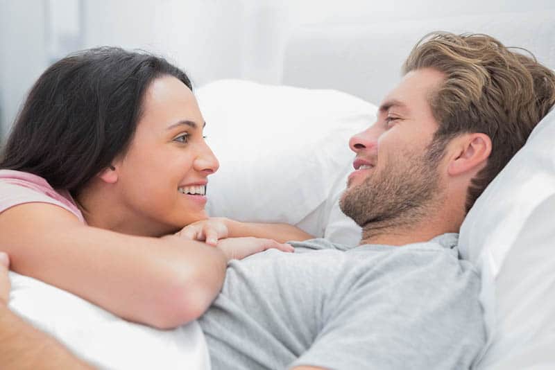 casal sorridente deitado na cama