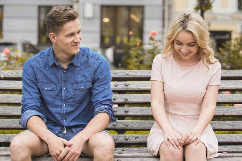 smiling shy couple sitting on the park bench