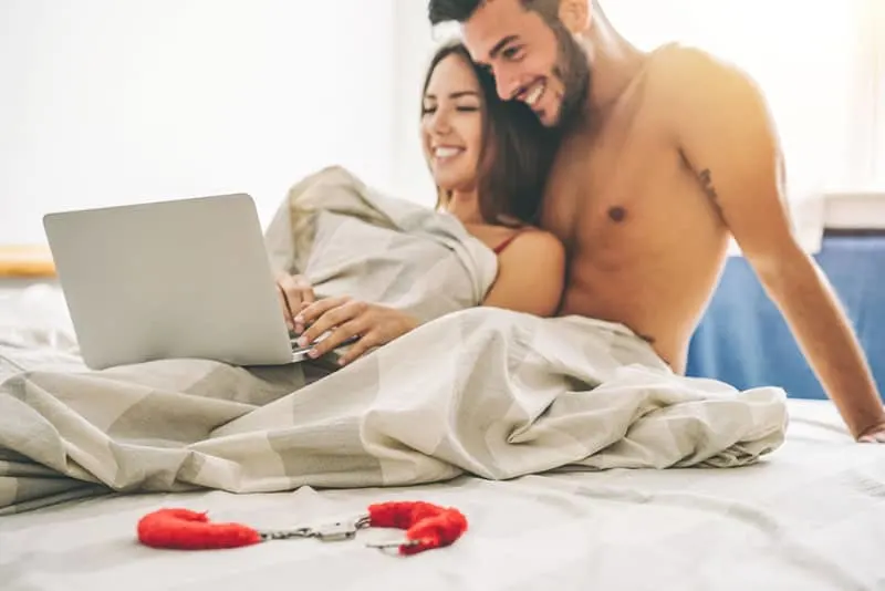 topless couple looking laptop on the bed