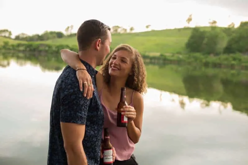 woman holding beer bottle while hugging a guy