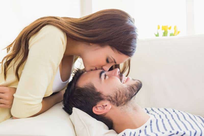 woman kissing man on forehead at home in living room