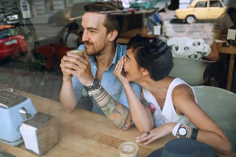 woman laughing at man while sitting at cafe