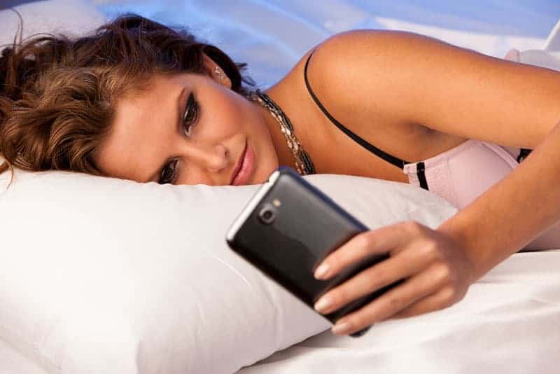 woman lying on bed and typing on her phone