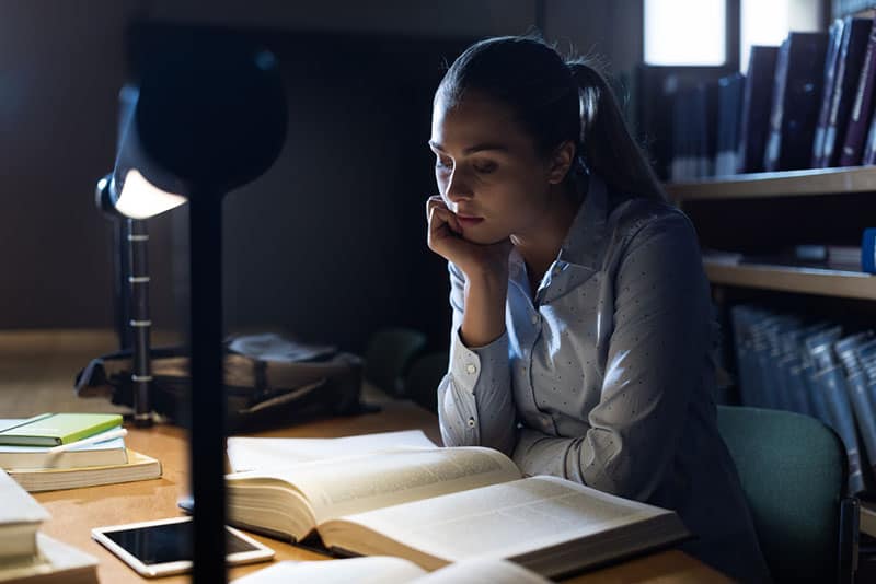  kvinne leser fra bok med lampe hjemme