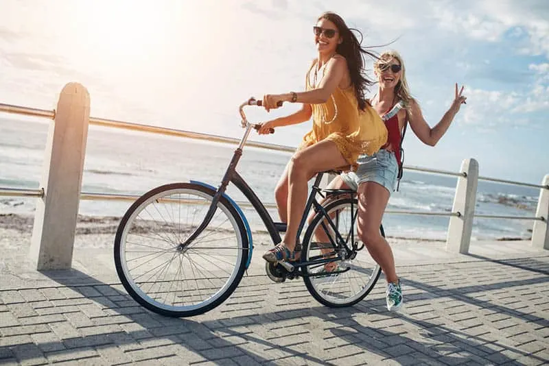 woman riding bike while her female friend is on back of bike