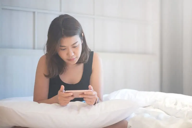woman sitting on bed and looking at her phone