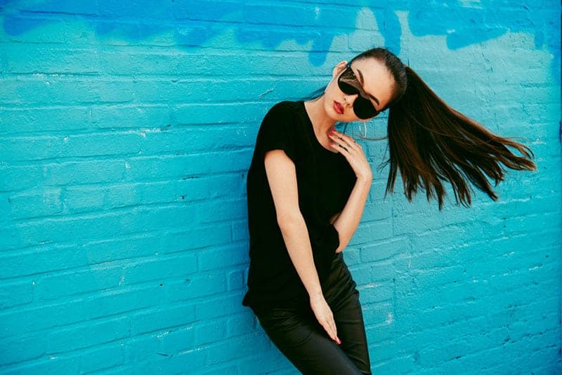 woman wearing sunglasses leaning on blue wall