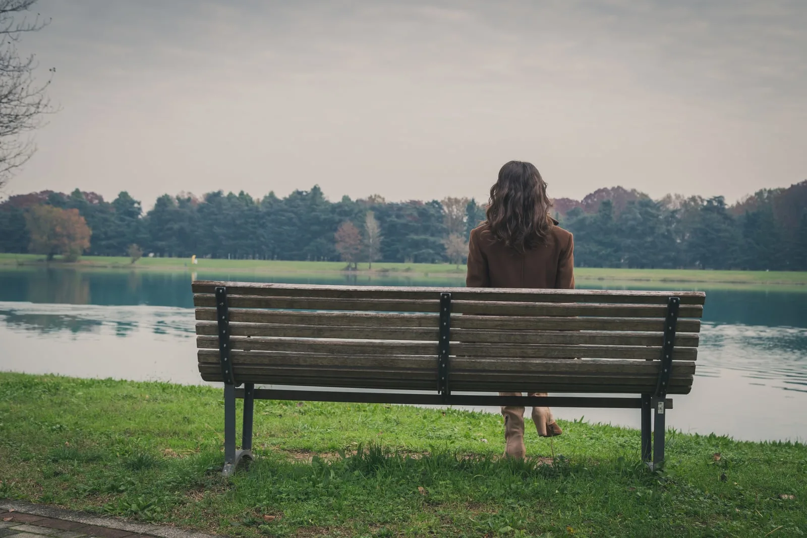 woman with long hair sitting on a bench in a city park
