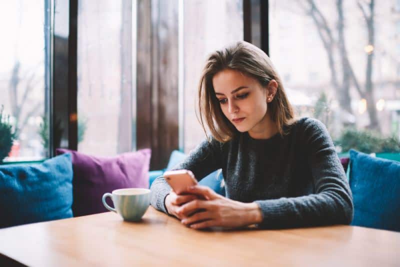 jong meisje zit aan koffiebar en kijkt naar telefoonscherm