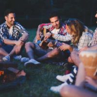 happy friends sitting beside bonfire