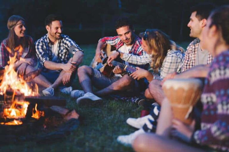 happy friends sitting beside bonfire