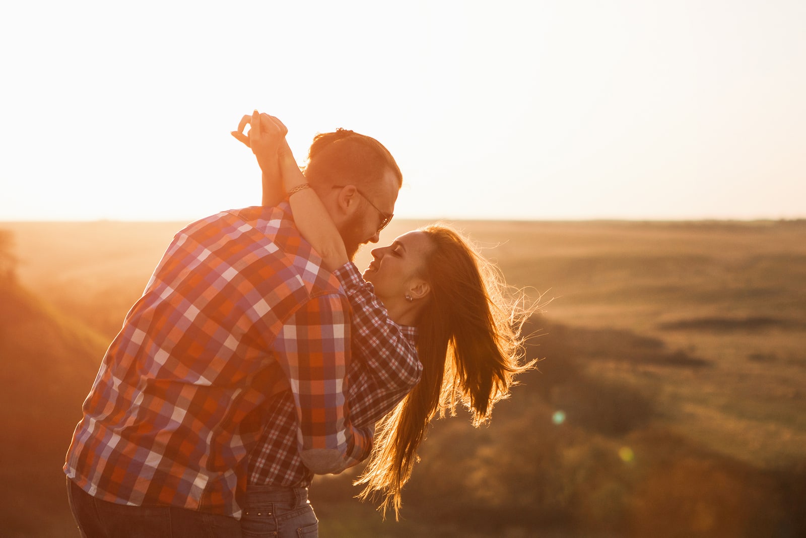 a man and a woman hugging and kissing at sunset in a field